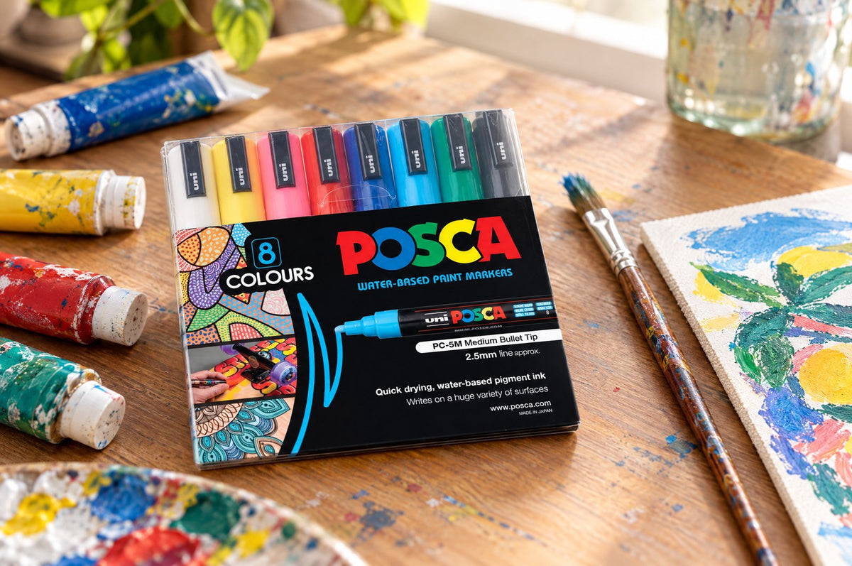 POSCA PC-5M markers beside acrylic paints on an art desk