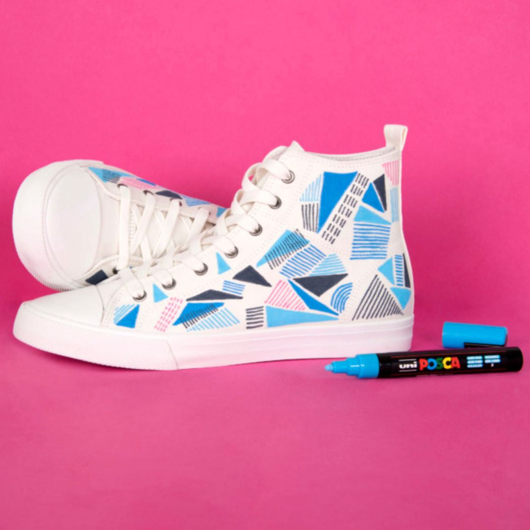 White high top sneakers decorated with blue, navy and pink geometric designs using a blue POSCA paint marker on a bright pink background