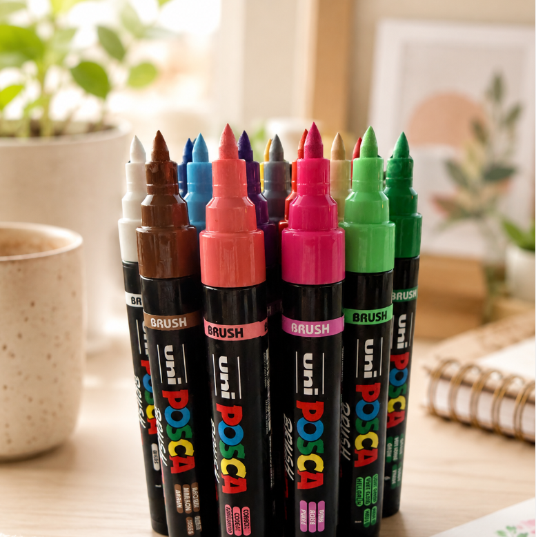 POSCA PC-5BR brush markers in assorted colours on a creative desk