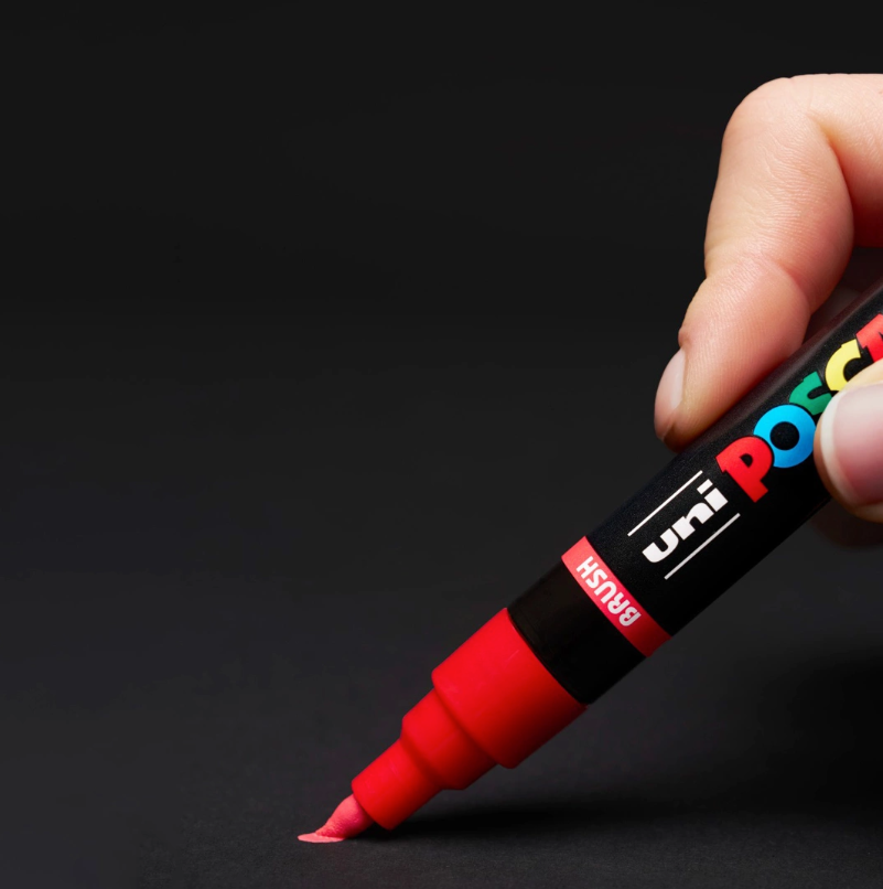 Red POSCA PC-5BR brush marker in use on a dark surface